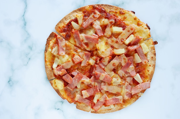 Foto deliciosa pizza com abacaxi, fatia de presunto, fatia de bacon, queijo mussarela, molho de pizza no fundo de mármore branco