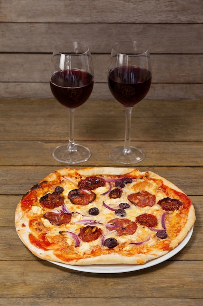 Deliciosa pizza con copas de vino tinto.