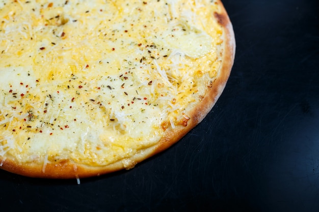Deliciosa pizza de cuatro quesos con queso cheddar, parmesano, mozzarella y salsa de tomate sobre un fondo negro. Vista desde arriba.
