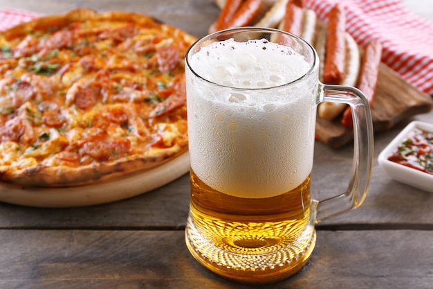 Deliciosa pizza de salsichas grelhadas e copo de cerveja na mesa de madeira close-up