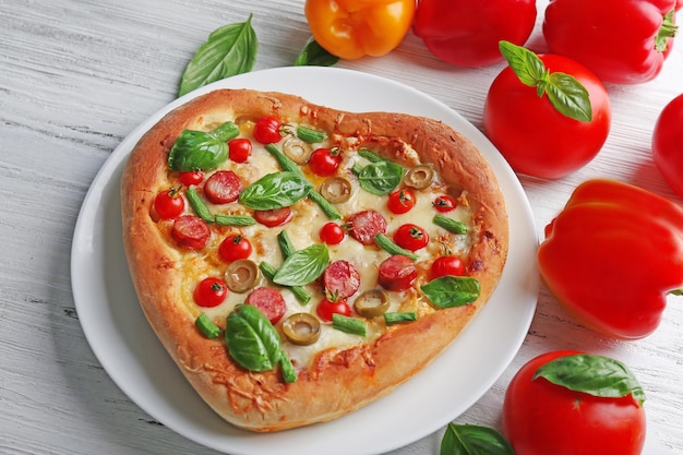 Deliciosa pizza en forma de corazón con verduras sobre fondo de madera de cerca