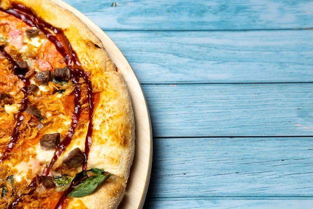 Deliciosa pizza grande com bacon e espinafre em um fundo azul de madeira.