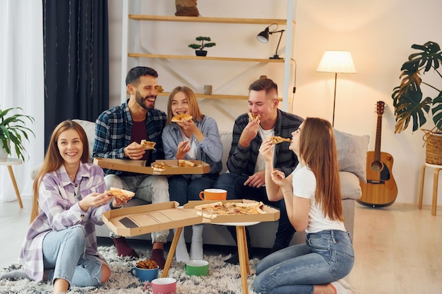 Con deliciosa pizza Grupo de amigos hacen fiesta juntos en el interior