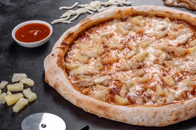 Deliciosa pizza italiana fresca com frango, tomate e abacaxi em um fundo escuro de concreto. cozinha italiana