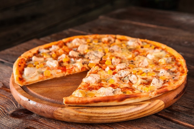 Deliciosa pizza italiana quente com frango, milho e queijo fatiado e servido na mesa de madeira. Foto do menu.