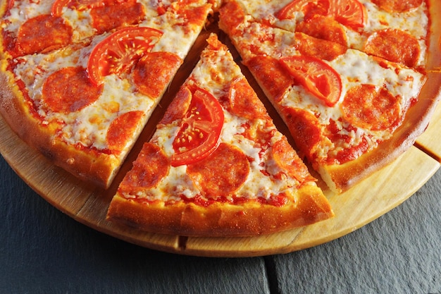 Deliciosa pizza de pepperoni y tomate en tablero de madera