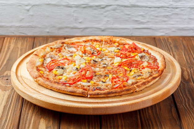 Deliciosa pizza con pollo, champiñones, queso, tomates y maíz sobre un fondo de madera.