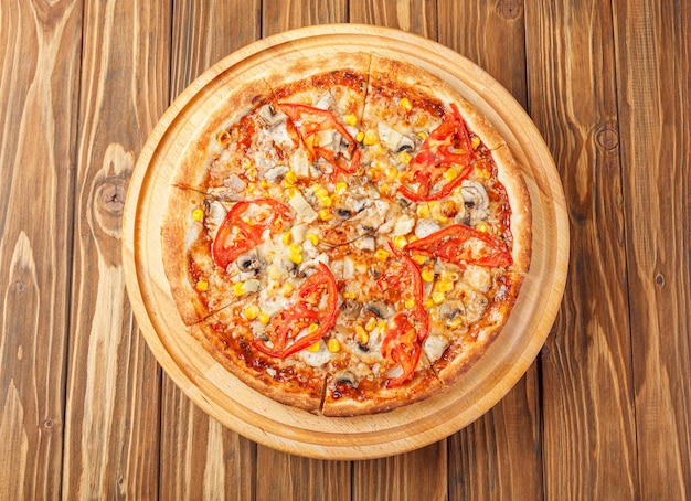 deliciosa pizza con pollo, setas, queso, tomates y maíz en un primer plano de fondo de madera