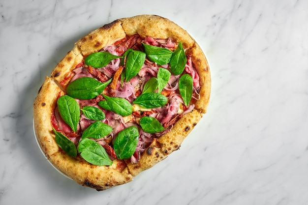 Deliciosa pizza con rosbif, tomates secos, cebollas en escabeche, queso y espinacas en un plato blanco sobre una superficie de mármol blanco