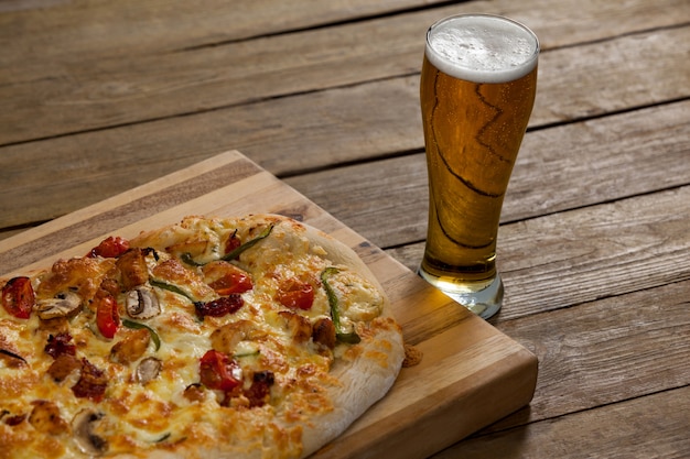 Deliciosa pizza servida sobre tabla de madera con un vaso de cerveza