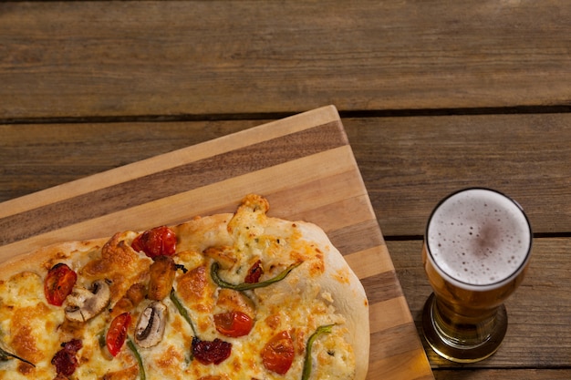 Deliciosa pizza servida sobre tabla de madera con un vaso de cerveza