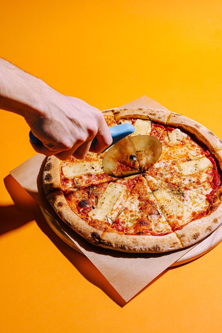 Deliciosa pizza siendo cortada con un cortador circular en un fondo amarillo vibrante
