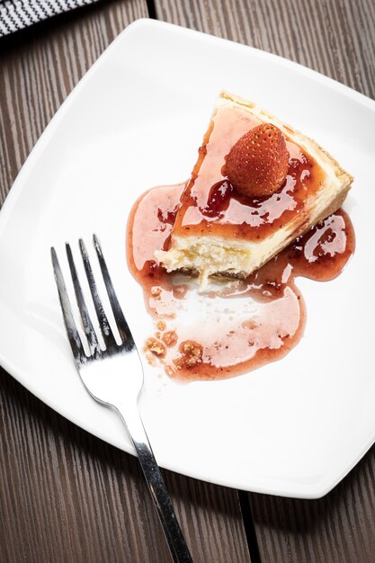 Deliciosa rebanada de tarta de queso con fresas en un plato blanco sobre una mesa de madera