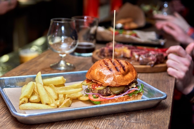 Deliciosa y sabrosa hamburguesa casera a la parrilla con carne, queso, tocino y salsa en la mesa de madera con espacio de copia. Manos sosteniendo hamburguesas con papas fritas y cerveza. Grupo de amigos comiendo comida rápida