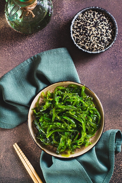 Deliciosa salada de algas wakame em um prato e sementes de gergelim em uma tigela e vista vertical