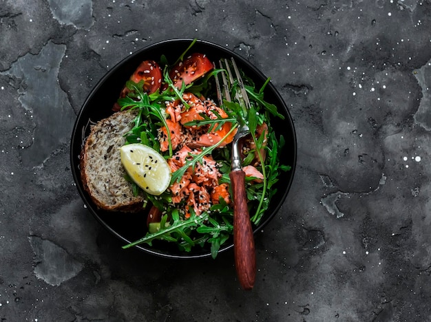 Deliciosa salada de dieta saudável com rúcula de salmão assado e legumes em uma vista superior de fundo escuro