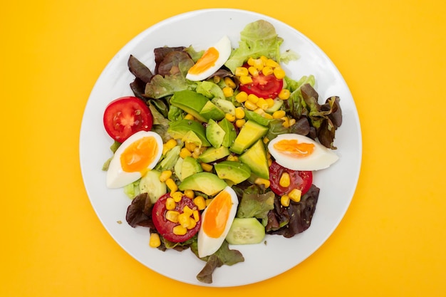 Foto deliciosa salada de vegetais leve feita de tomates, conservas de milho, pepino, alface, abacate e ovo.