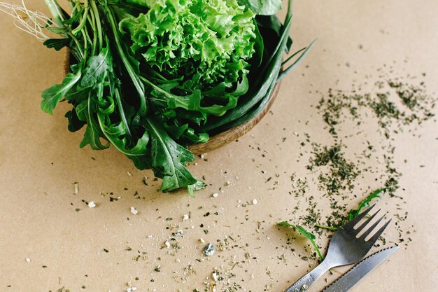 Deliciosa salada fresca de espinafre de rúcula em tigela de madeira e talheres em fundo artesanal