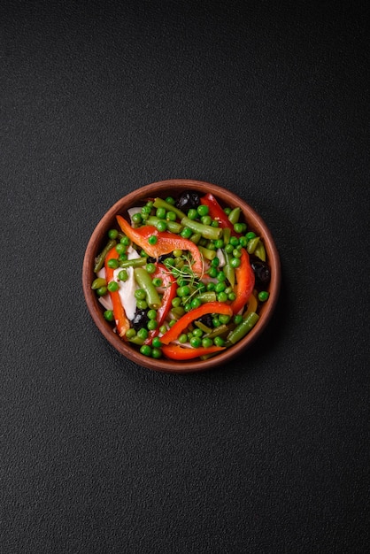 Deliciosa salada fresca de feijão verde, ervilha, pimentão e queijo com sal e especiarias sobre um fundo escuro de concreto