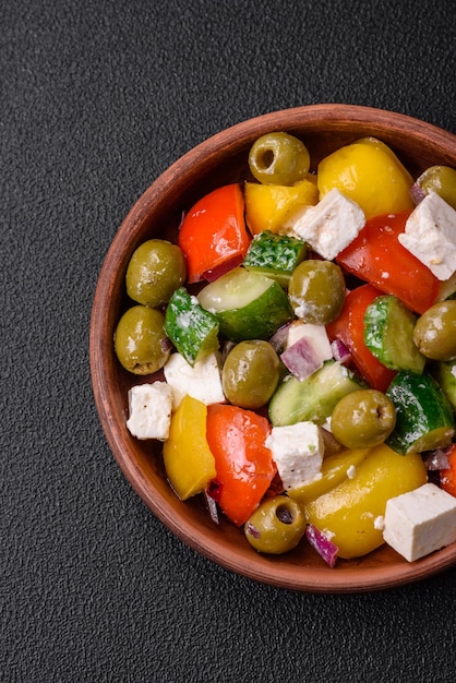 Deliciosa salada grega fresca e suculenta com queijo feta, azeitonas, tomate, pepino, pimenta, sal e especiarias sobre um fundo escuro de concreto