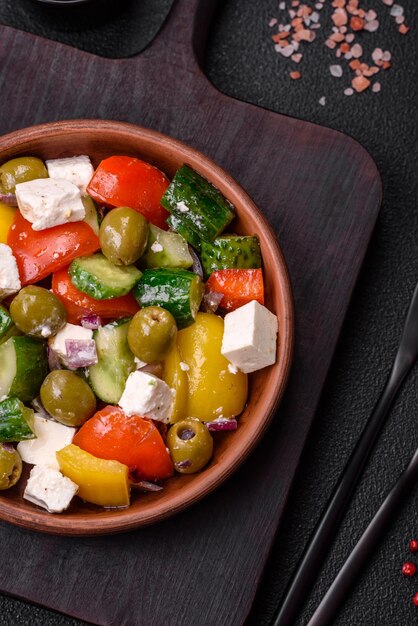 Deliciosa salada grega fresca e suculenta com queijo feta, azeitonas, tomate, pepino, pimenta, sal e especiarias sobre um fundo escuro de concreto