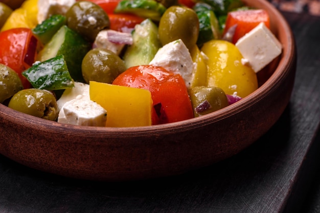 Deliciosa salada grega fresca e suculenta com queijo feta, azeitonas, tomate, pepino, pimenta, sal e especiarias sobre um fundo escuro de concreto