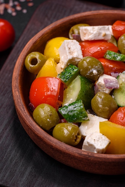 Deliciosa salada grega fresca e suculenta com queijo feta, azeitonas, tomate, pepino, pimenta, sal e especiarias sobre um fundo escuro de concreto