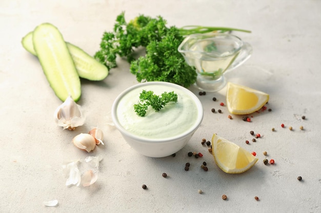 Deliciosa salsa de yogur en un cuenco con ingredientes sobre un fondo gris