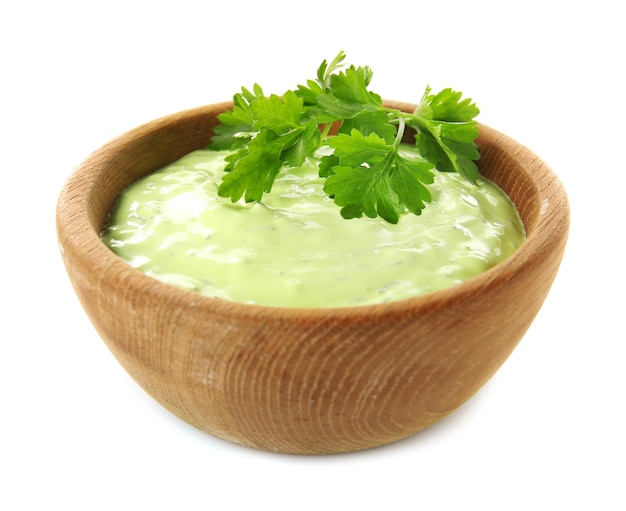 Deliciosa salsa de yogur con hojas de perejil en un tazón de madera aislado en blanco