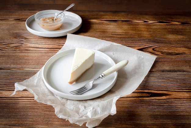 Deliciosa sobremesa doce bolo de queijo clássico fatia de Nova York em fundo rústico de madeira Fatia de bolo saboroso no prato cerâmico servido com garfo de sobremesa e geléia de maçã