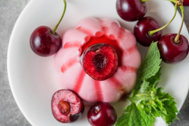 Deliciosa sobremesa panna cotta de cereja com molho de frutas frescas de cereja e hortelã em um prato na mesa cinza Vista superior