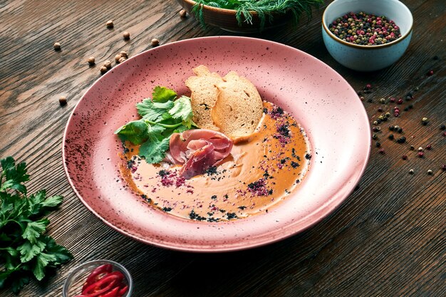 Deliciosa sopa de crema de coco y lentejas con picatostes y jamón en una placa roja sobre una mesa de madera. Comida de restaurante. Vista cercana