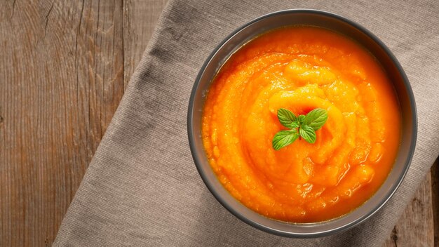 Deliciosa sopa de abóbora e cenoura em tigela na velha mesa de madeira