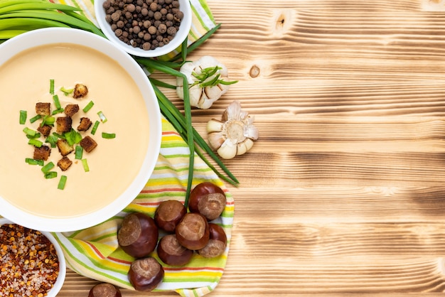 Deliciosa sopa de castanhas com croutons e ervas em uma mesa de madeira. Vista do topo. Copie o espaço.