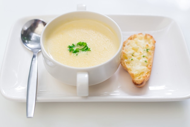 Deliciosa sopa de maíz en un tazón blanco servido con pan.