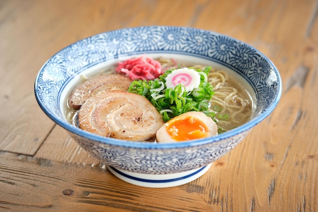 Deliciosa sopa de ramen con huevo blando hervido y carne de cerdo chashu servida en un cuenco colocado en una mesa de madera contra un fondo borroso