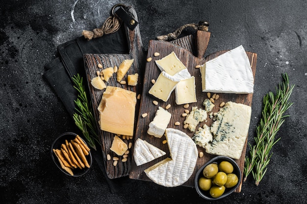 Deliciosa Tábua de Queijos. Variedade de queijos, camembert, brie, gorgonzola, parmesão, azeitonas, nozes e ervas. Fundo preto. Vista do topo.