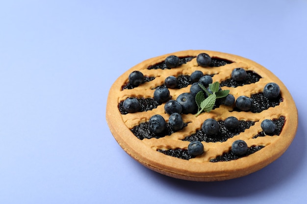 Deliciosa tarta de arándanos con frutos rojos sobre fondo violeta