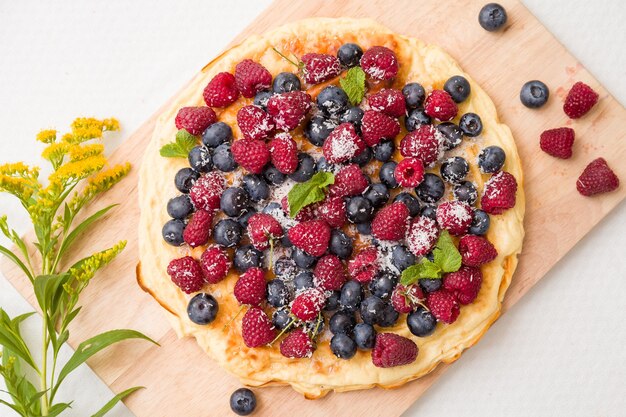 Deliciosa tarta casera con frambuesas y arándanos orgánicos y flores de verano sobre tabla de madera