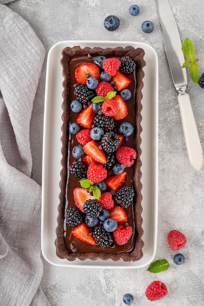 Foto deliciosa tarta de crema de chocolate con bayas frescas y menta en la parte superior en el plato sobre un fondo gris