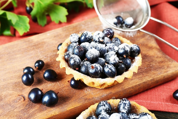 Deliciosa tarta crujiente con grosellas negras en el primer plano de la tabla de cortar de madera