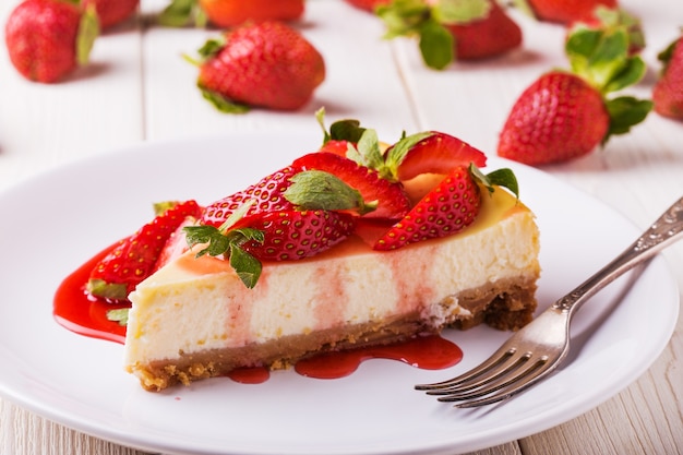 Deliciosa tarta de queso casera con fresas en mesa de madera blanca.