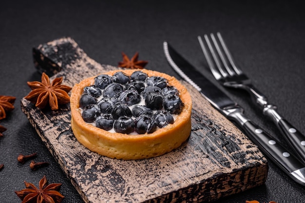 Deliciosa tarta redonda dulce fresca con arándanos maduros y crema sobre un fondo de hormigón oscuro