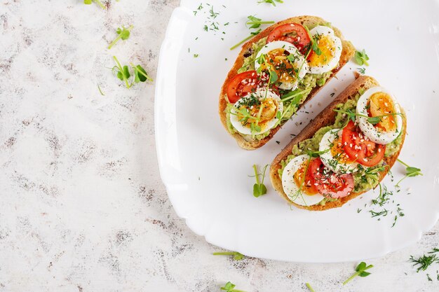 Foto deliciosa tostada con aguacate, tomates de huevo hervido y microgreen en un plato blanco, desayuno saludable, comida de dieta ceto, comida de moda, vista superior.