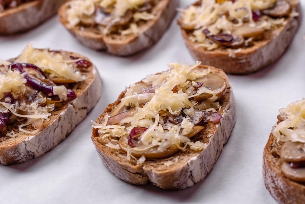 Deliciosa tostada crujiente o bruschetta con champiñones de cebolla frita y queso con especias y hierbas sobre un fondo de hormigón oscuro