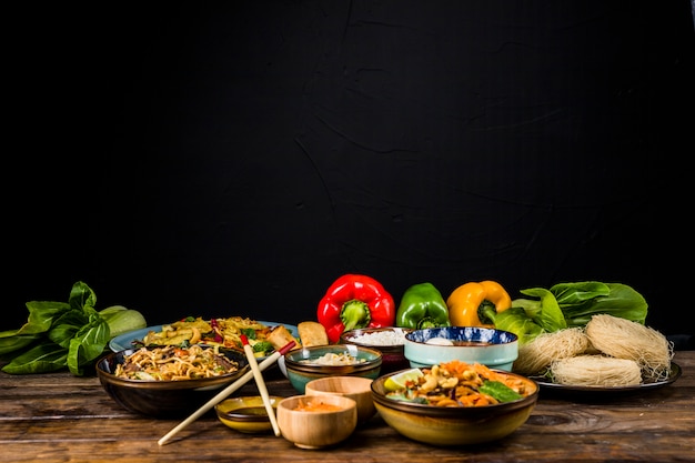 Deliciosa variedad de comida tailandesa en diferentes tazones con bokchoy y pimientos en una mesa con fondo negro