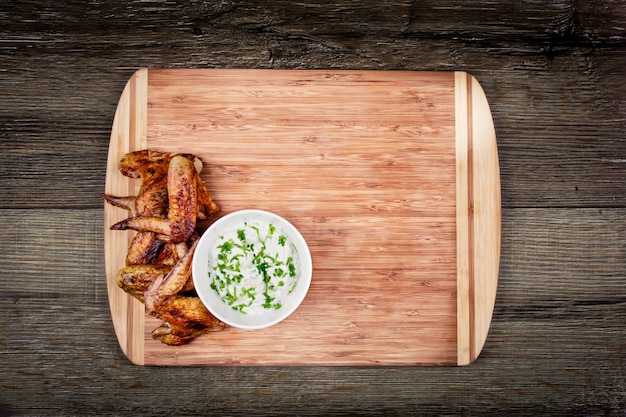 Deliciosas alitas de pollo a la parrilla con salsa de ajo en una tabla de cortar en madera rústica con vista superior de copyspace