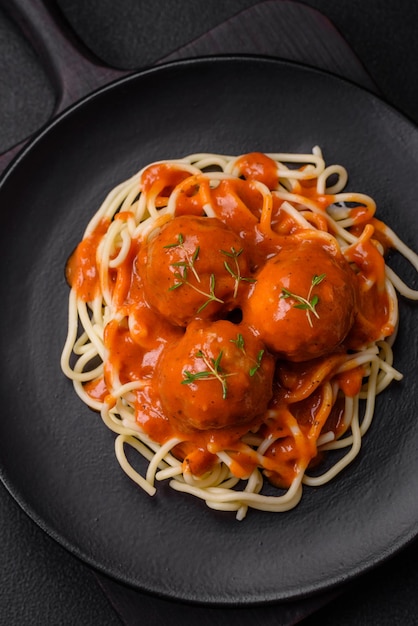 Deliciosas almôndegas frescas e massas em molho de tomate com especiarias salgadas e ervas em um fundo escuro de concreto