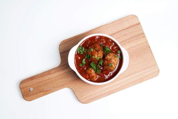 Deliciosas almôndegas suculentas em molho de tomate picante. A tigela fica em uma tábua de servir de madeira. Vista do topo.