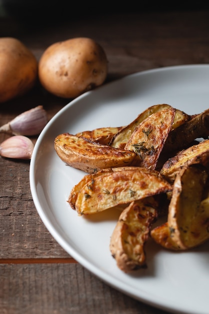 Deliciosas batatas assadas do campo em um grande prato branco com especiarias, endro e cebolinha em uma mesa de madeira